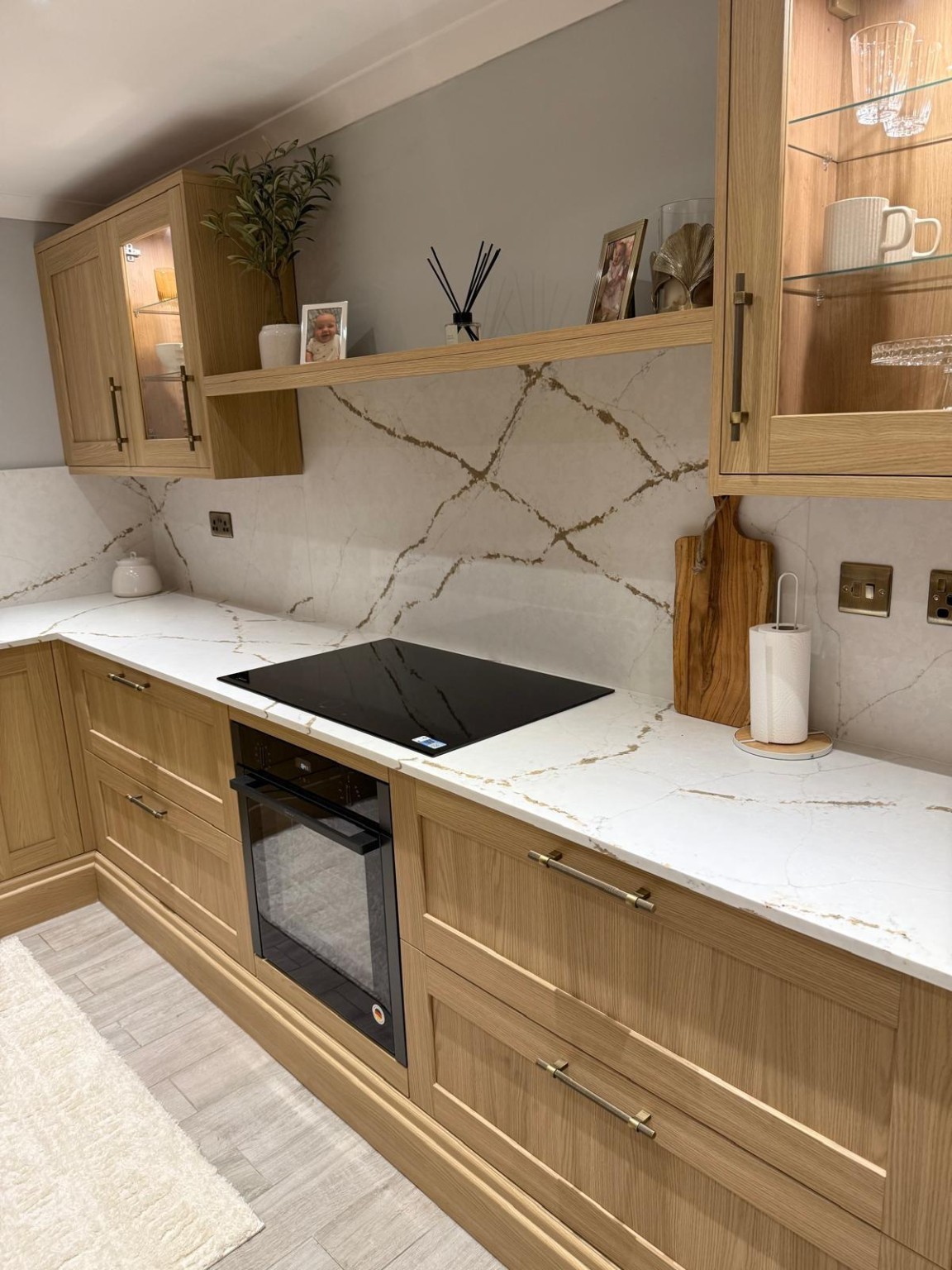 Oak kitchen with brass handles, illuminated glass cabinets, integrated hob and marble-effect splashback